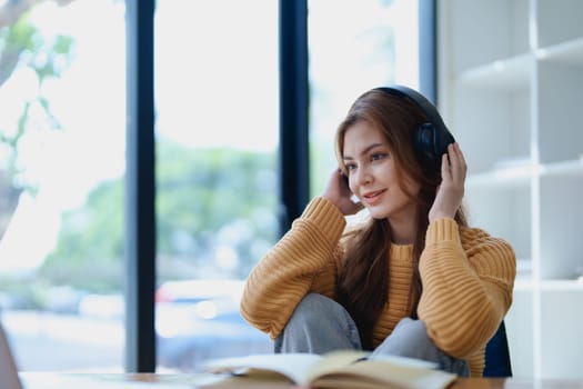 Young woman enjoying a relaxing music break at her desk while using headphones, writing in a notebook, and working on her laptop for calm inspiration.
