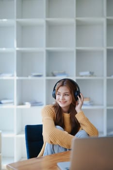 Young woman enjoying a relaxing music break at her desk while using headphones, writing in a notebook, and working on her laptop for calm inspiration.