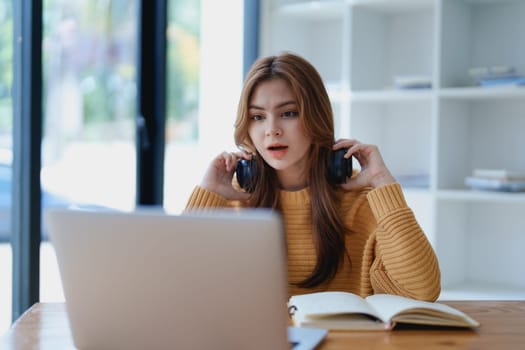 Young woman enjoying a relaxing music break at her desk while using headphones, writing in a notebook, and working on her laptop for calm inspiration.