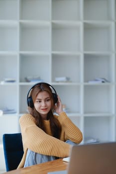 Young woman enjoying a relaxing music break at her desk while using headphones, writing in a notebook, and working on her laptop for calm inspiration.
