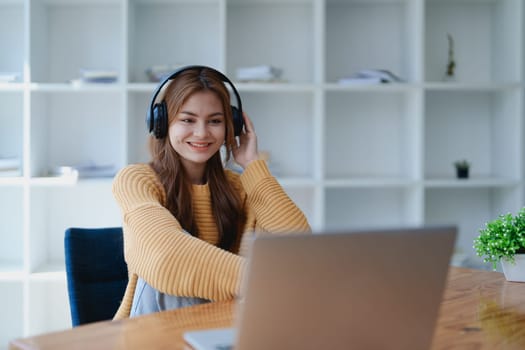 Young woman enjoying a relaxing music break at her desk while using headphones, writing in a notebook, and working on her laptop for calm inspiration.