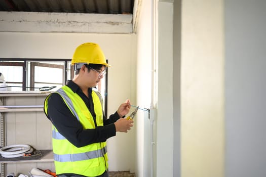 Electrician wearing yellow hard hat working on wall wiring at a construction site.