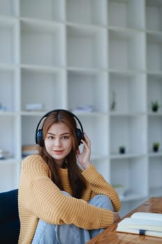 Young woman enjoying a relaxing music break at her desk while using headphones, writing in a notebook, and working on her laptop for calm inspiration.