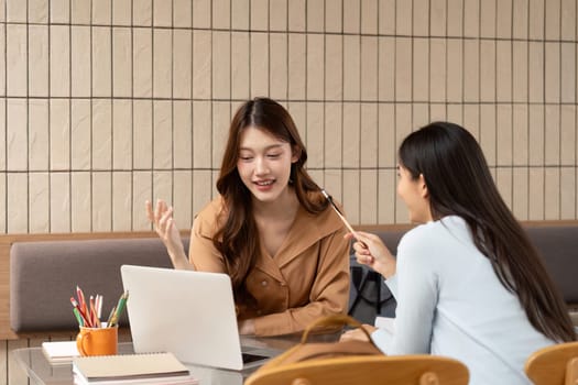In an open study area, two friends utilize modern technology to enhance their learning experience, discussing various subjects while sharing laughs.