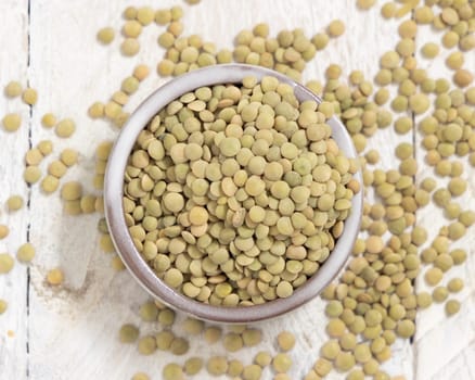 Small bowl full of dried green lentils on white table top view. Healthy vegetarian food, legumes plant-based protein source. Traditional mediterranean raw uncooked cousin ingredient