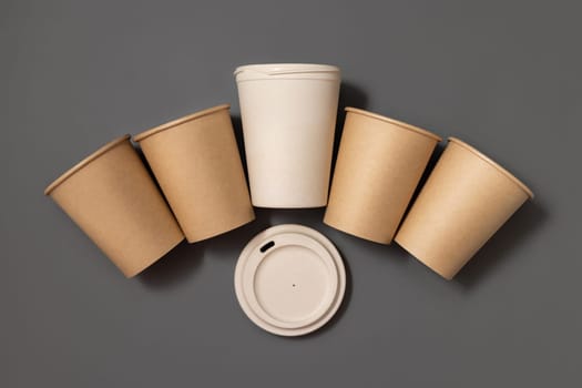 Disposable new beige kraft paper cups and opened reusable bamboo coffee cup with a lid on gray top view, mockup with copy space. Empty coffee cups. No plastic and sustainable lifestyle concept