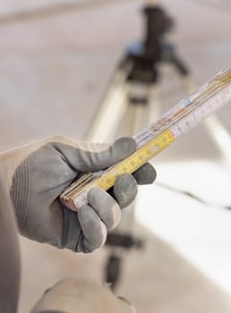 Craftsman in dusty glove holding a folded rule against horizontal rotary laser level. Engineer during measurement work, construction or renovation site