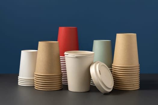 Disposable new multicolor paper cups and opened reusable bamboo coffee cup on gray and blue closeup, mockup with copy space. Empty coffee cups. No plastic and sustainable lifestyle concept