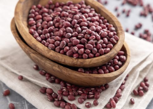 Wooden bowls full of dried red azuki beans on folded napkin on gray table closeup. Vegetarian protein source from legumes. Traditional East Asian cousin ingredient