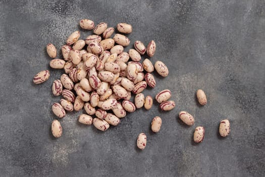 Pile of dried pinto beans on gray table top view. Healthy vegetarian food, legumes protein source. Traditional Latin American cousin ingredient