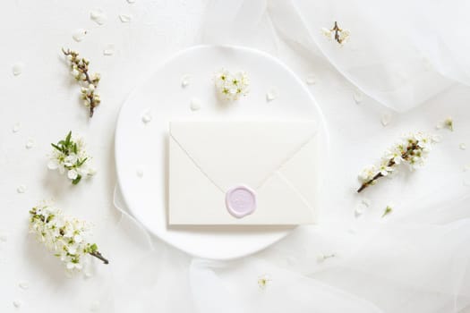 Sealed envelope on plate near tulle and wild plums white flowers top view, mockup. Pastel horizontal card for spring party design, mothers day or romantic wedding stationery
