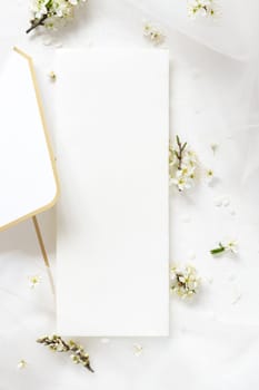 Blank menu card on envelope near tulle and wild plums white flowers top view, mockup. Pastel vertical card for spring party design or romantic wedding stationery, Close to nature or mothers day