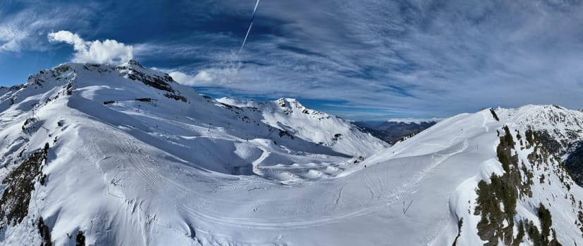 A breathtaking aerial view of a beautiful winter landscape with snow-covered alpine mountains, sunny skies, and scenic slopes perfect for skiing, snowboarding, hiking, and outdoor adventures