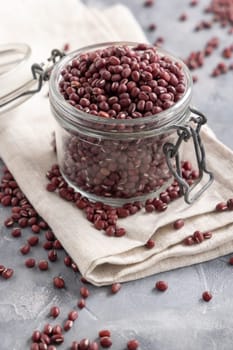 Opened glass jar full of dried red azuki beans on folded napkin on gray table closeup. Vegetarian protein source from legumes. Traditional East Asian cousin ingredient