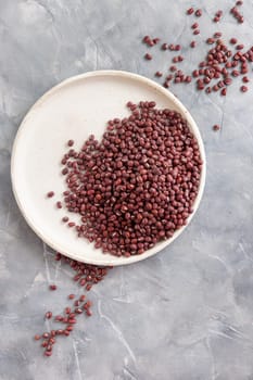 Ceramic plate full of dried red azuki beans on gray table top view, copy space. Healthy vegetarian food, legumes protein source. Traditional East Asiancousin ingredient