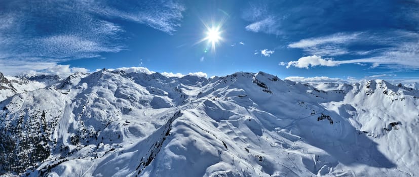 A breathtaking aerial view of a beautiful winter landscape with snow-covered alpine mountains, sunny skies, and scenic slopes perfect for skiing, snowboarding, hiking, and outdoor adventures