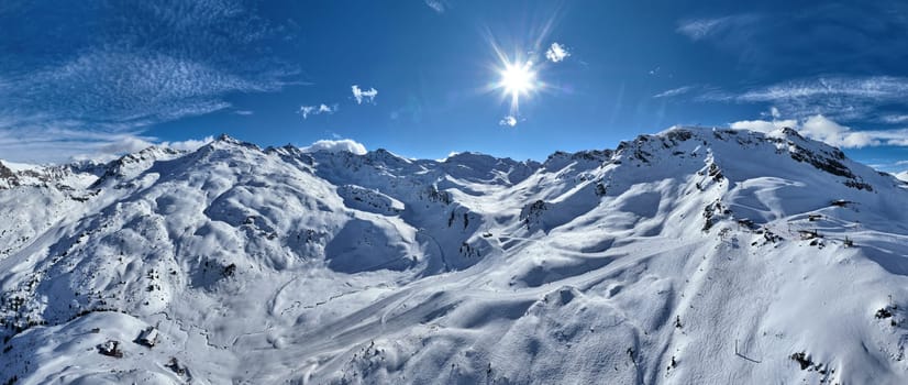 A breathtaking aerial view of a beautiful winter landscape with snow-covered alpine mountains, sunny skies, and scenic slopes perfect for skiing, snowboarding, hiking, and outdoor adventures