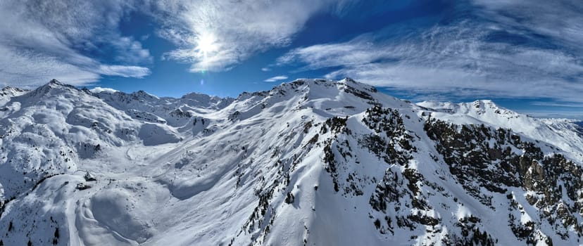 A breathtaking aerial view of a beautiful winter landscape with snow-covered alpine mountains, sunny skies, and scenic slopes perfect for skiing, snowboarding, hiking, and outdoor adventures