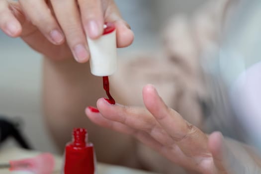 The woman carefully applies a red nail polish, emphasizing her attention to detail and love for colorful nail art. This image captures a moment of self-grooming and personal flair.