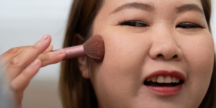 A close-up of a woman applying blush to her cheeks, showcasing her focus on achieving a flawless finish in her beauty routine.
