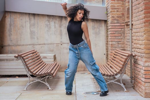 African American woman dancing in a creative pose between benches in an urban setting. She wears casual clothes and shows balance, strength, and expression. Concept of movement, art, and freedom.