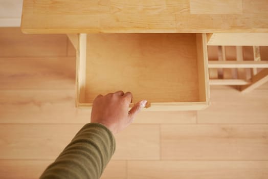 A hand is opening a wooden drawer in a bright, minimalistic space.