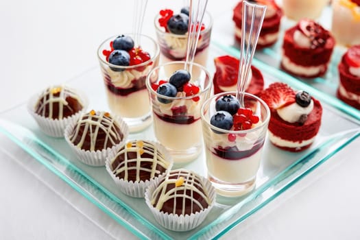 A colorful array of sweet treats is presented on a glass platter, featuring creamy desserts topped with berries and elegant chocolate truffles, perfect for celebrating an occasion.