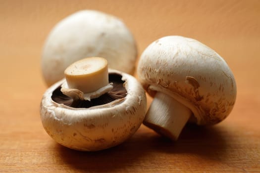 Three fresh white mushrooms are displayed on a wooden surface, highlighting their smooth caps and stems. Natural light accentuates their texture, inviting culinary inspiration.