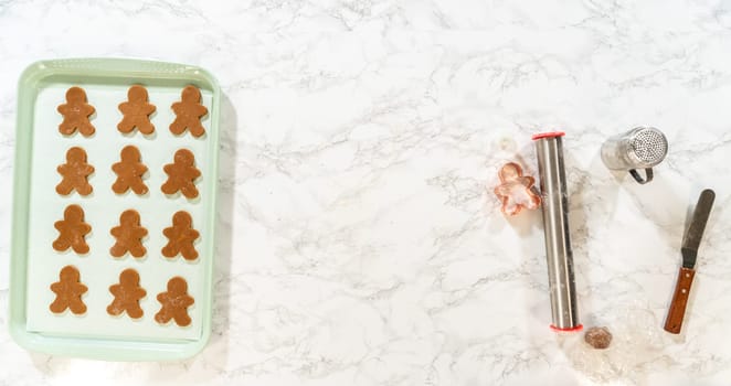 A green baking sheet with unbaked gingerbread man-shaped Classic Gingerbread Cookies is placed on a marble countertop, captured from a top-down angle.