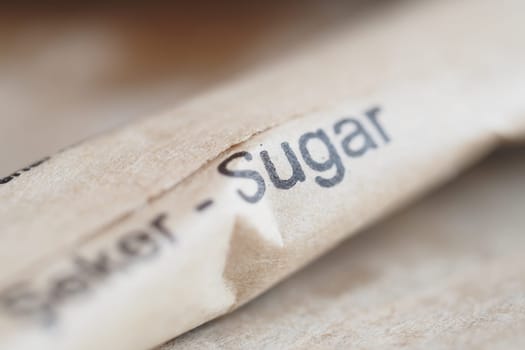 Close-up of a sugar packet resting on a wooden table surface.