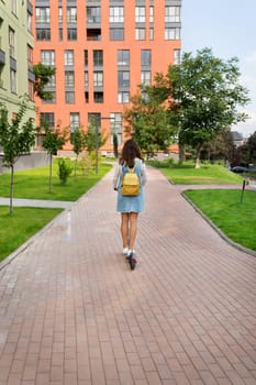 A young woman with a backpack rides an electric scooter along a paved path in a modern residential area.