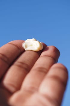 Person holds a dollop of cream in hand under bright blue sky.