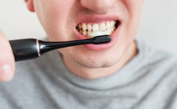 A young man diligently brushes his teeth with an electric toothbrush, showcasing healthy oral hygiene practices.