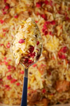 Spoonful of flavorful biryani topped with colorful saffron and rose petals