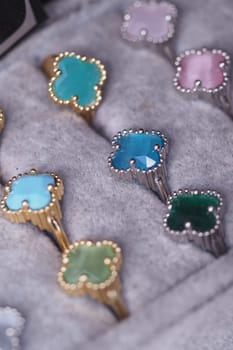 Various gemstone rings in shades of blue, green, and pink are neatly arranged.