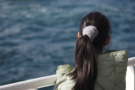 A young girl stands by the railing, observing the serene ocean waves.
