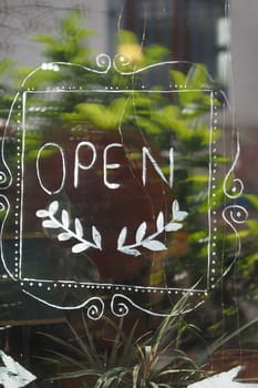 A hand-painted open sign is visible on a window surrounded by plants.