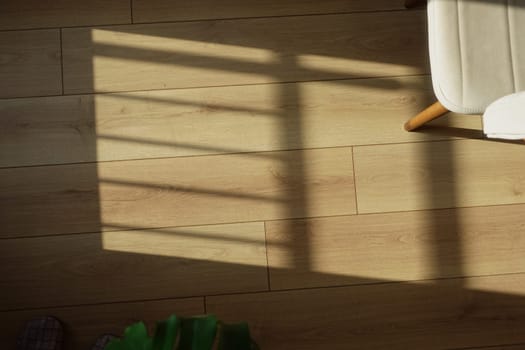 Sunlight creates patterns on a wooden floor while a chair rests nearby.