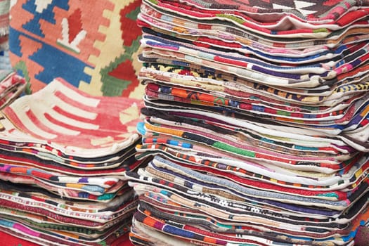 Handwoven textiles are neatly stacked in a market, showcasing bright colors.