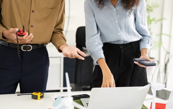 Two professionals engage in collaborative project planning, discussing energy-efficient designs while using tools like a calculator and measuring devices.