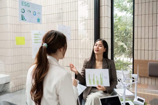 In a collaborative workspace, two professionals engage in a conversation about ESG strategies, showcasing data charts that reflect their commitment to sustainability.