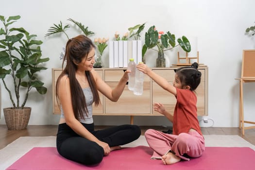 In a lively atmosphere, a mother and daughter make hydration fun as they exchange a water bottle, embodying an active lifestyle filled with laughter.