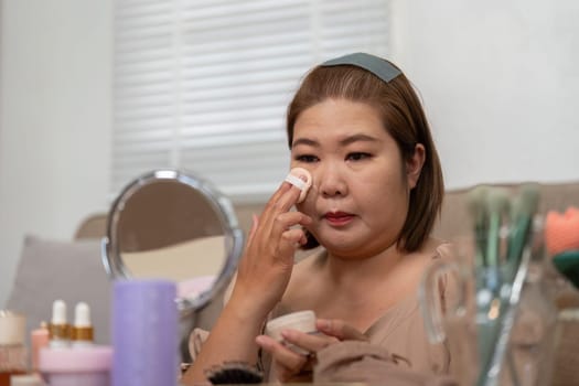A woman sits in her cozy space, applying foundation with a sponge, showcasing her dedication to a beauty routine and enhancing her natural features.