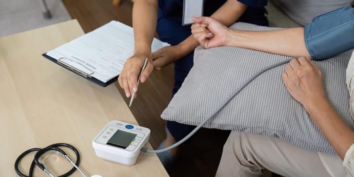 A dedicated caregiver measures the blood pressure of an elderly woman in a comfortable home environment, showcasing the importance of periodic health checks.