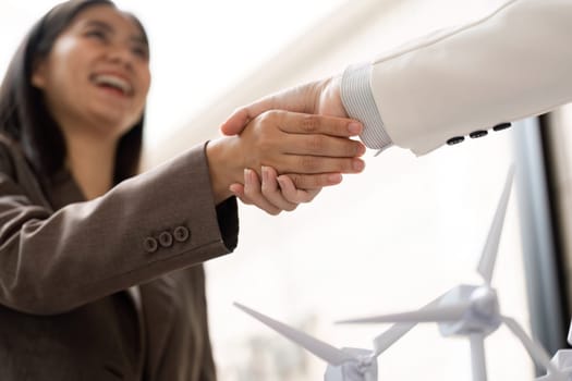 Two professionals engage in a friendly handshake, representing a commitment to sustainability and ESG initiatives, with wind turbine models symbolizing their joint effort.