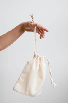 Hand holding beige drawstring pouch against neutral background.