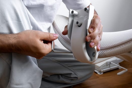 Male assembling office chair using allen wrench in bright room.