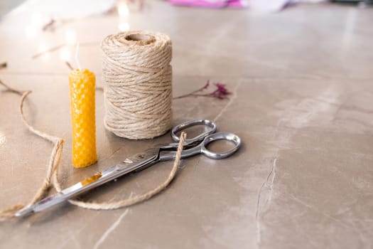 Crafting essentials. Twine, scissors, wax candle on marble surface.