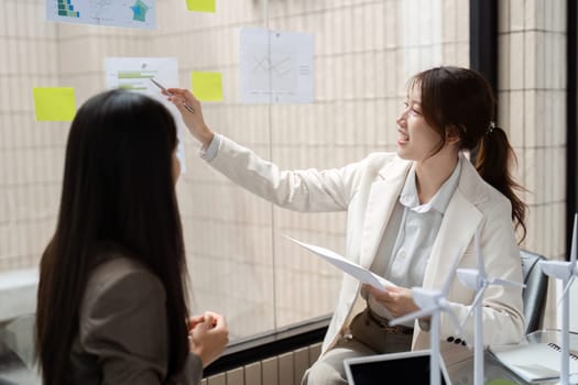 Two women brainstorm sustainable solutions for their business, utilizing modern tools and a collaborative approach to achieve their goals in an eco-friendly setting.