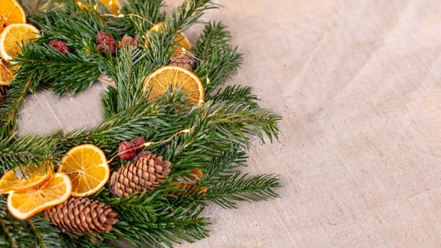 Wide banner with natural spruce wreath. Rustic Christmas table decor, with natural spruce wreath, dried oranges, pine cones on a fabric tablecloth. Copy space